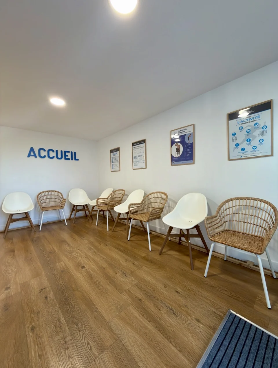L'accueil du cabinet : chaises blanches et en rotin, parquet, affiches sur le sport et le lettrage Accueil en bleu